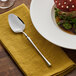 An Acopa Hepburn stainless steel spoon on a yellow napkin next to a plate of food.
