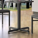 A Lancaster Table & Seating black stamped steel table base with a wood panel top.