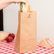 A hand holding a sandwich in a Duro brown paper bag.