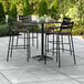 A black Lancaster Table & Seating bar table with four black chairs on an outdoor patio.