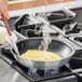 A person cooking an omelette in a Choice aluminum non-stick fry pan on a stove.