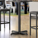 A black Lancaster Table & Seating bar height table base with leveling feet.