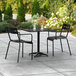 A black Lancaster Table & Seating outdoor table and chairs on a patio.