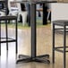 A close-up of a black Lancaster Table & Seating bar height table base with leveling feet.