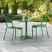 A green Lancaster Table & Seating outdoor table with two chairs on a patio.