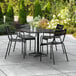 A Lancaster Table & Seating black outdoor table with chairs on a patio with a black umbrella.