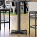 A close-up of a black Lancaster Table & Seating bar height column table base with leveling feet.