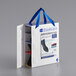 A white box with a blue handle and blue ribbon with a package of Shoes For Crews CrewGuard overshoes inside.