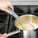 A hand using a Vollrath stainless steel whisk to stir a white liquid in a pot on a stove.