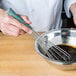 A person using a Vollrath stainless steel whisk to mix brown liquid in a bowl.