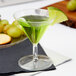 A clear plastic Fineline Tiny Tini filled with green liquid and a lime slice on the rim.