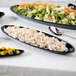 A table with black oval melamine platters filled with food including salad.
