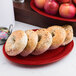 A red Carlisle oval melamine platter with bagels and apples on it.