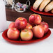A red Carlisle oval melamine platter with a pile of apples on it.