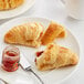A plate with two White Toque Butter Croissants and strawberry jam on the side.