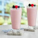 Two glasses of pink Capora mixed berry smoothies with berries on top.