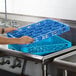A person holding a blue Carlisle glass rack extender over a metal sink.