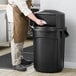 A man in a chef's uniform cleaning a Rubbermaid trash can.
