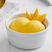 A white bowl of yellow Acai Roots Mango Cream Sorbet with a spoon.