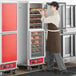 A man in a brown apron taking food out of an Avantco holding cabinet with clear Dutch doors.