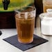 A Cambro Laguna clear plastic tumbler filled with brown liquid and ice sits on a napkin.