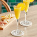 Two Acopa Select trumpet flute glasses of orange juice and a slice of orange on a table.