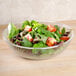 A Cambro pebbled serving bowl filled with salad with tomatoes and spinach on a table.