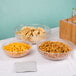 A table with Cambro pebbled serving bowls filled with chips, goldfish crackers, and pretzels.