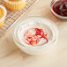 A cupcake with swirls of red and white frosting in a yellow wrapper with a bowl of red liquid.