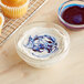 A glass bowl of blue and white swirled frosting next to a cupcake on a cooling rack.