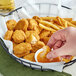 A hand dipping a Tindle Plant-Based Vegan Chicken Nugget into a bowl of french fries.