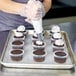 A person in gloves decorating Rich's Allen Un-Iced Chocolate Cupcakes on a tray.