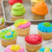 A group of cupcakes with colorful frosting, including blue, yellow, and green, with Rich's Bettercreme Everyday Variety Whipped Icing.