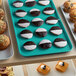 A green Cambro market tray of pastries, muffins, and cookies on a counter.