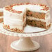 A Rich's Allen un-iced round carrot cake with a slice missing on a white cake stand.
