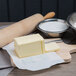 A block of salted butter on a cutting board with a rolling pin and a bowl of flour.