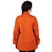 A woman wearing an orange Uncommon Chef long sleeve chef coat with mesh back.