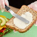 A person spreading Follow Your Heart Reduced Fat Vegenaise on a sandwich.