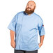 A man wearing a sky blue Uncommon Chef short sleeve chef coat with a mesh back.