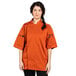 A woman wearing an orange Uncommon Chef short sleeve chef coat with black buttons.