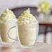 A close-up of two glasses of white Capora White Chocolate Frappe mix with whipped cream.