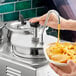 A person using a ServSense stainless steel pump to pour cheese sauce on a bowl of chips.