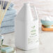 A white plastic jug of Nourish Lemongrass Body Wash with a green label next to a stack of towels.