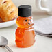A clear plastic bear-shaped container of honey with a black lid next to a spoon.