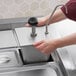 A hand using a ServSense stainless steel pump to fill a metal container on a metal tray.
