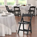 A black Lancaster Table & Seating vinyl seat for a folding chair on a chair next to a table.
