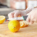 A person in green gloves using a Schraf serrated edge paring knife to cut a lemon.