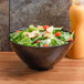 A black round catering bowl filled with salad on a wood surface.