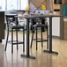 A Lancaster Table & Seating white birch and ash bar table with a black base and two black stools.