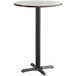A round bar table with a white birch surface and black base.